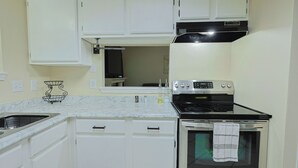 A kitchen with white cabinets, a black stove, and a microwave above it. - Willow Tree House - Private Cinema (Houston)