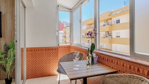 En balkon med et bord, stole, en potteplante og udsigt til omkringliggende bygninger.
