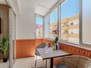 Ein Balkon mit Tisch, Stühlen, einem Blumentopf und Blick auf benachbarte Gebäude.