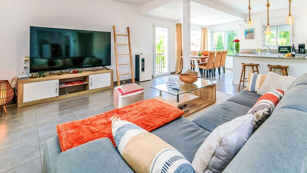 Ein modernes Wohnzimmer mit einem großen Flachbildfernseher, einem Glastisch und einer Couch mit gemusterten Kissen.