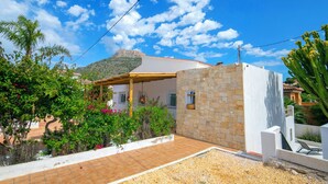 Ein Haus mit einer Steinmauer, einer gefliesten Terrasse und einem Berg im Hintergrund.