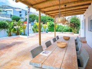 A covered outdoor dining area with a long wooden table, wicker chairs, and a hanging light fixture. - Bohemia by Interhome (Calpe/Calp)