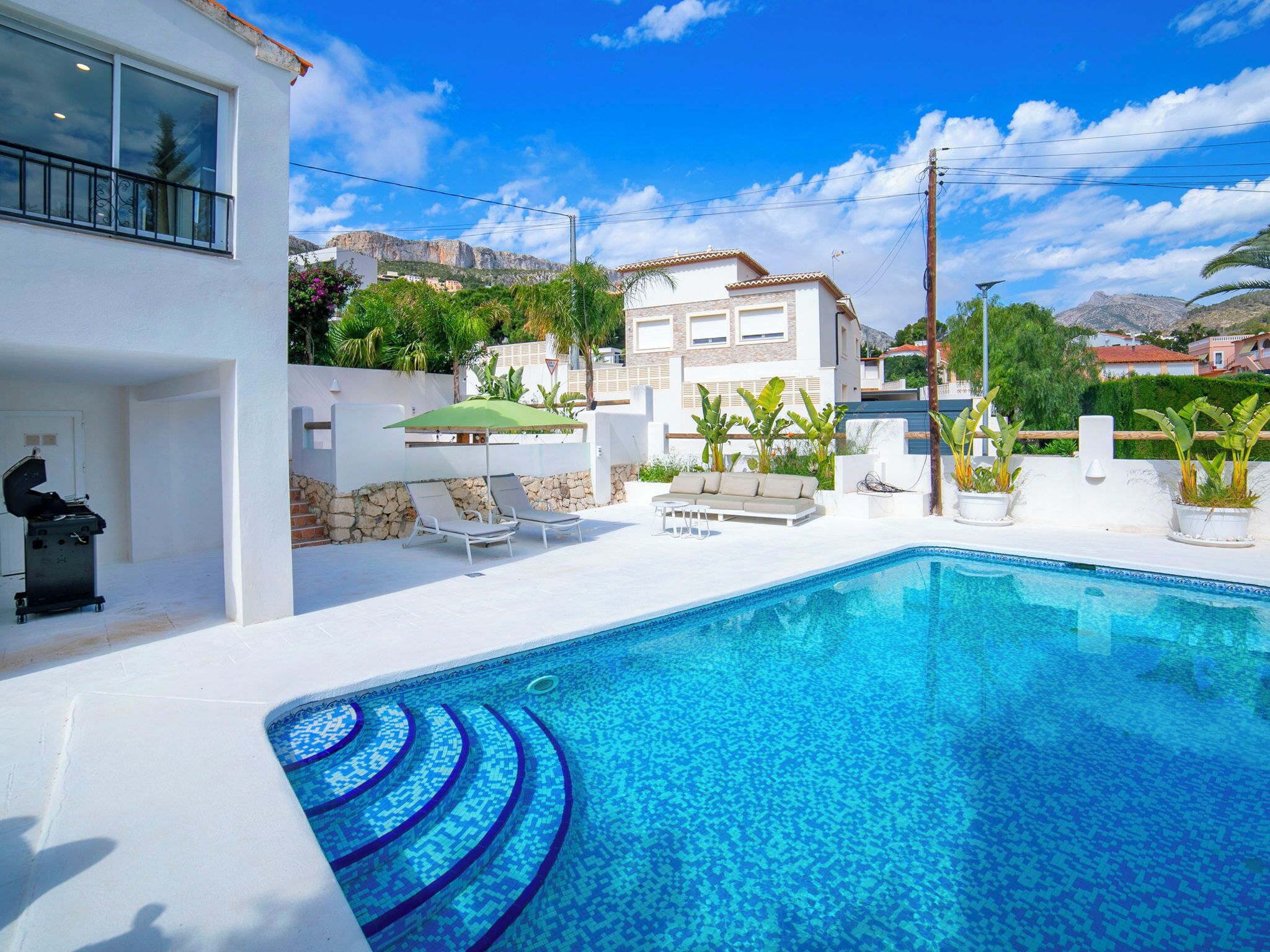 Un área de piscina moderna con una piscina azul cristalina, sillas de descanso y una parrilla.