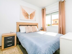 A bedroom with a bed, a nightstand, a drawer unit, a window with curtains, and a wall-mounted artwork. - Bohemia by Interhome (Calpe/Calp)