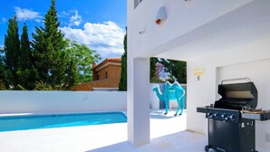 Ein Poolbereich mit Grill, einer Kameldekoration und Blick auf Bäume sowie ein Gebäude.