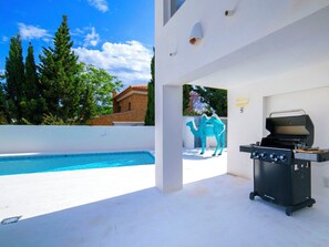 A poolside area with a barbecue grill, a camel decoration, and a view of trees and a building. - Bohemia by Interhome (Calpe/Calp)
