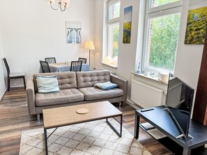 Ein Wohnzimmer mit Sofa, Couchtisch, Fernseher und einem Essbereich mit Stühlen und Tisch.