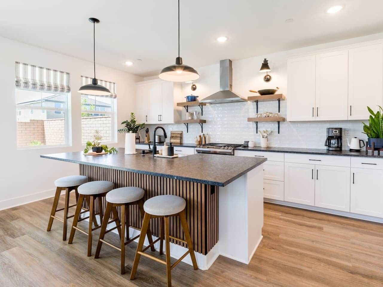 A modern kitchen with a central island, bar stools, pendant lighting, and white cabinetry.
