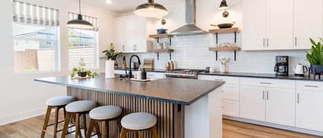 A modern kitchen with a central island, bar stools, pendant lighting, and white cabinetry.