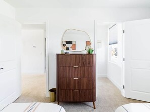 A room with a wooden dresser, a mirror, and a small plant on top. There are white doors and a carpeted floor. - Desert Oasis • Heated Pool & Spa • Sleeps 10 (Indio)