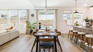 A spacious living area with a dining table, chairs, a sofa, and a kitchen area with bar stools. - Desert Oasis • Heated Pool & Spa • Sleeps 8 (Indio)