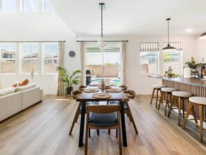 A spacious living area with a dining table, chairs, a sofa, and a kitchen area with bar stools. - Desert Oasis • Heated Pool & Spa • Sleeps 8 (Indio)