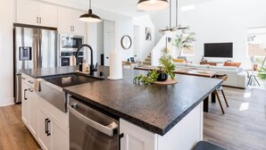 A modern kitchen with stainless steel appliances, a central island, pendant lighting, and a view into the living area. - Desert Oasis • Heated Pool & Spa • Sleeps 8 (Indio)