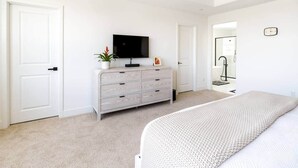 A bedroom with a bed, a dresser, a television, and a door. - Desert Oasis • Heated Pool & Spa • Sleeps 8 (Indio)