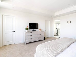A bedroom with a bed, a dresser, a television, and a door. - Desert Oasis • Heated Pool & Spa • Sleeps 8 (Indio)