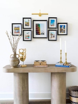 A wooden table with a vase, a decorative object, and books. There are framed pictures on the wall above the table. - Desert Oasis • Heated Pool & Spa • Sleeps 10 (Indio)