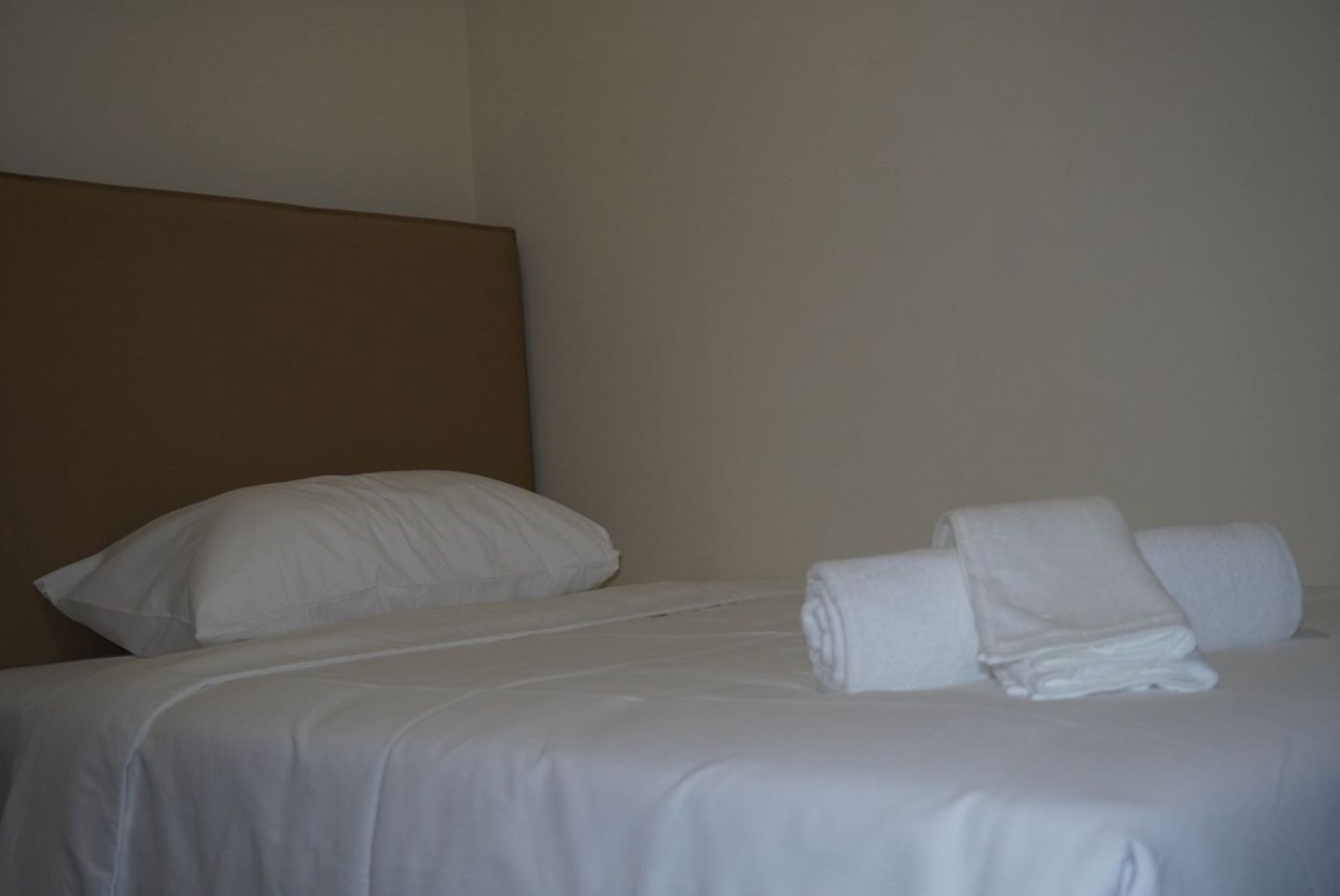Una cama bien hecha con sábanas y almohadas blancas, un cabecero y toallas enrolladas sobre la cama.