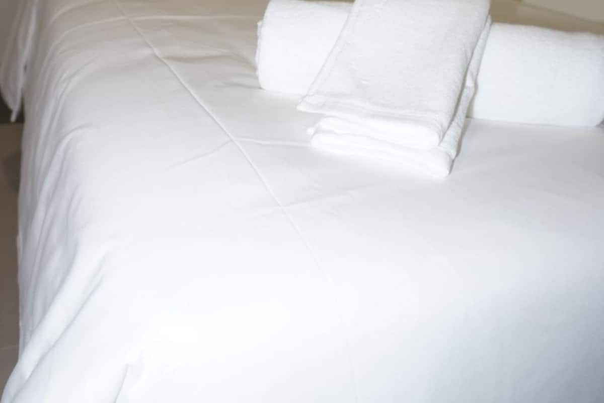 Una habitación de hotel con dos camas, cada una con ropa blanca y almohadas, y una pared lisa.
