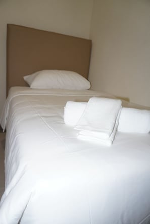 A hotel room with two beds, each with white linens and pillows, and a plain wall.