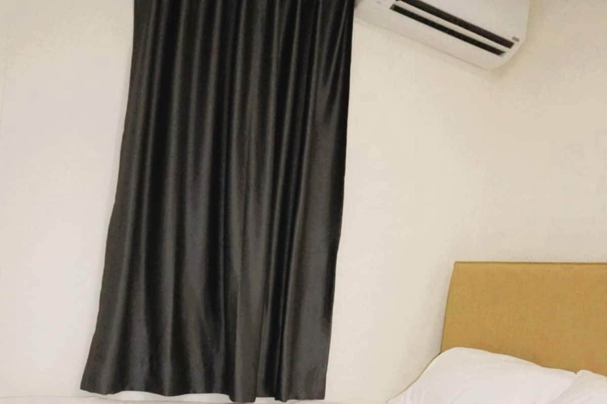 Habitación de hotel con una cama, ropa de cama blanca, cortina negra y aire acondicionado instalado en la pared.