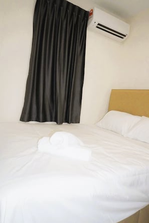 A hotel room with a bed, white linens, a black curtain, and a wall-mounted air conditioner.