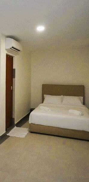 A hotel room with a bed, a door, and an air conditioning unit.