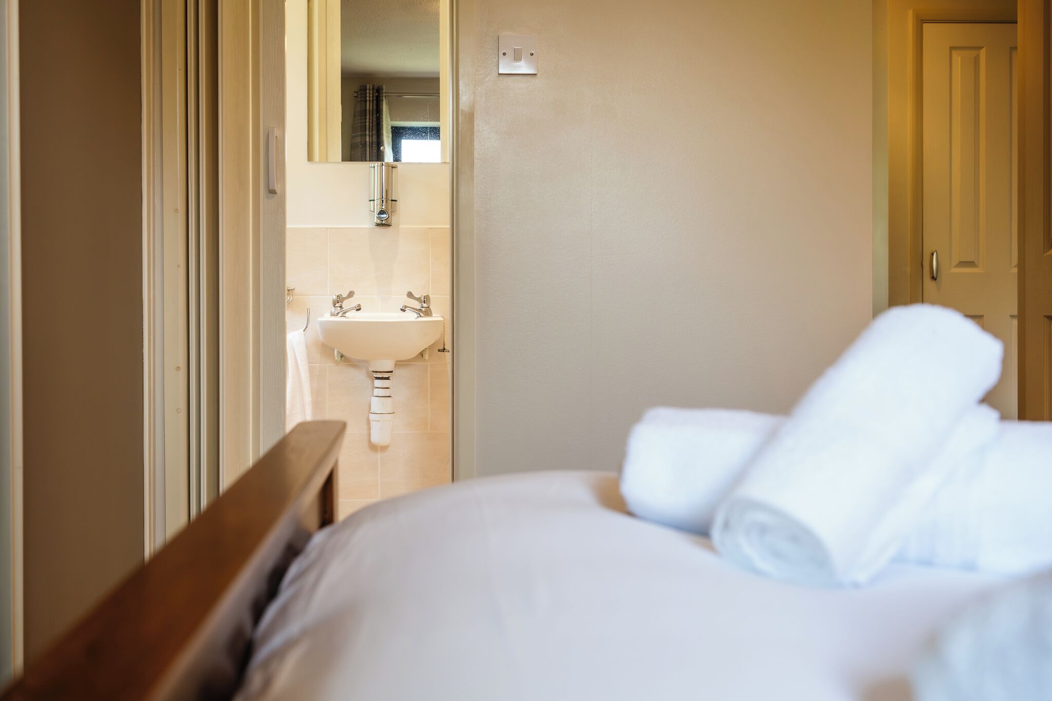 A hotel room with a bed, a wooden headboard, a white sink, and a mirror.