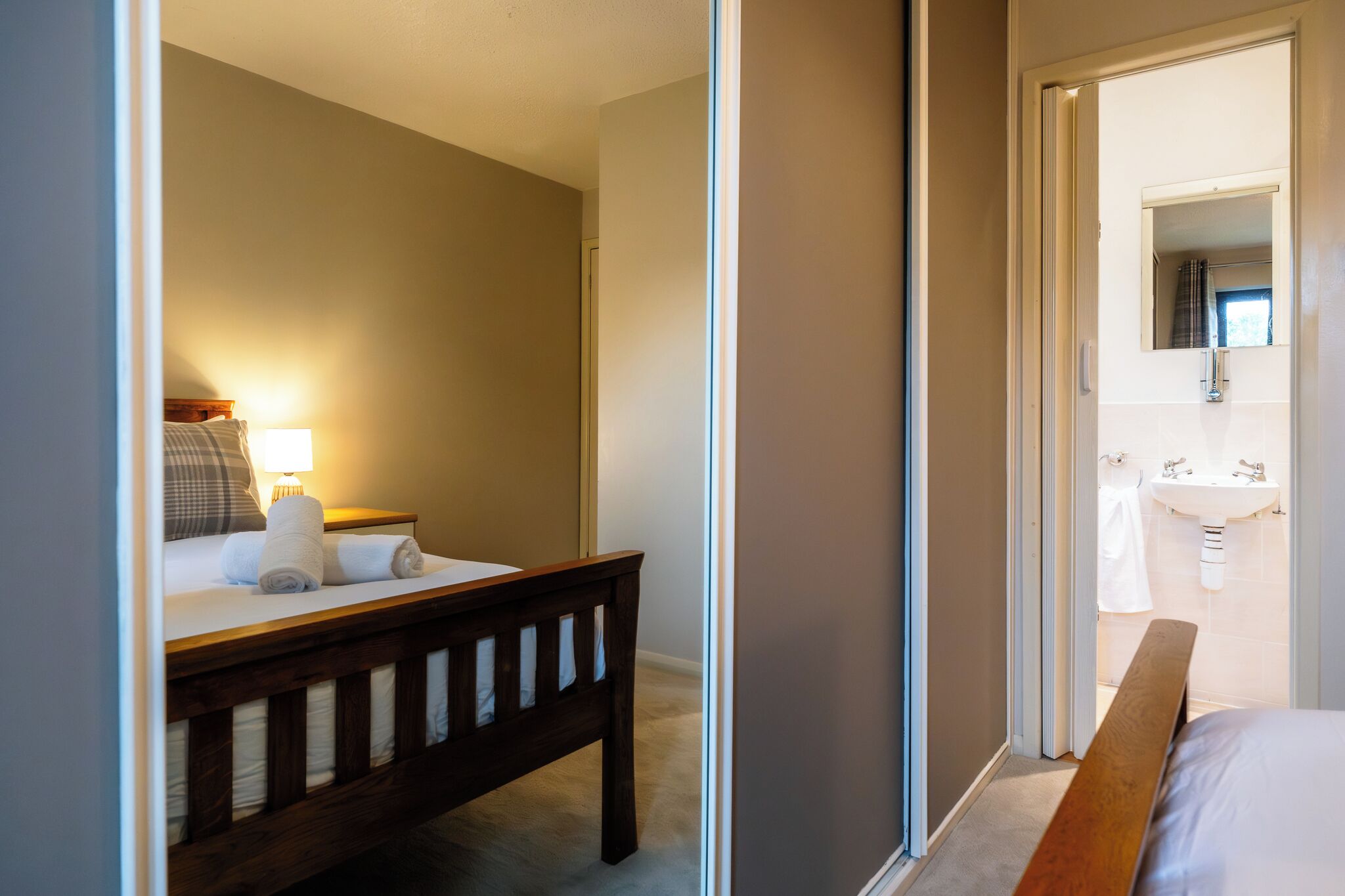 A hotel room with a bed, bedside table, lamp, and a view of the bathroom.