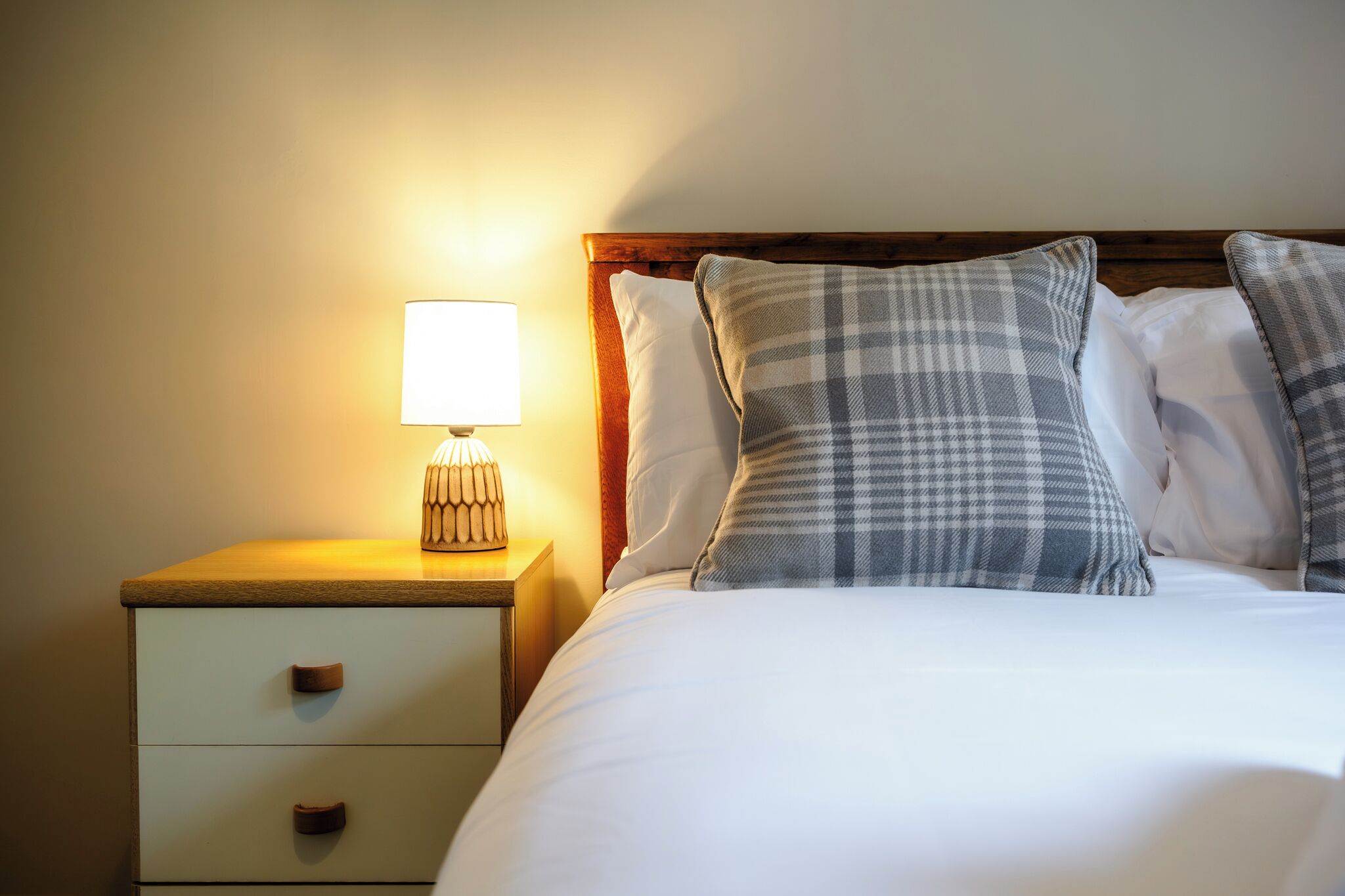A neatly made bed with a wooden headboard, a bedside lamp, and a nightstand with drawers.