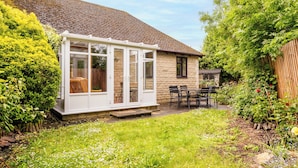 Una casa con veranda, patio con sedie e giardino con diverse piante.