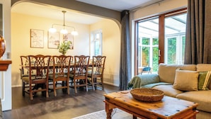 Zona pranzo con tavolo e sedie in legno, un lampadario e un'ampia finestra con tende.