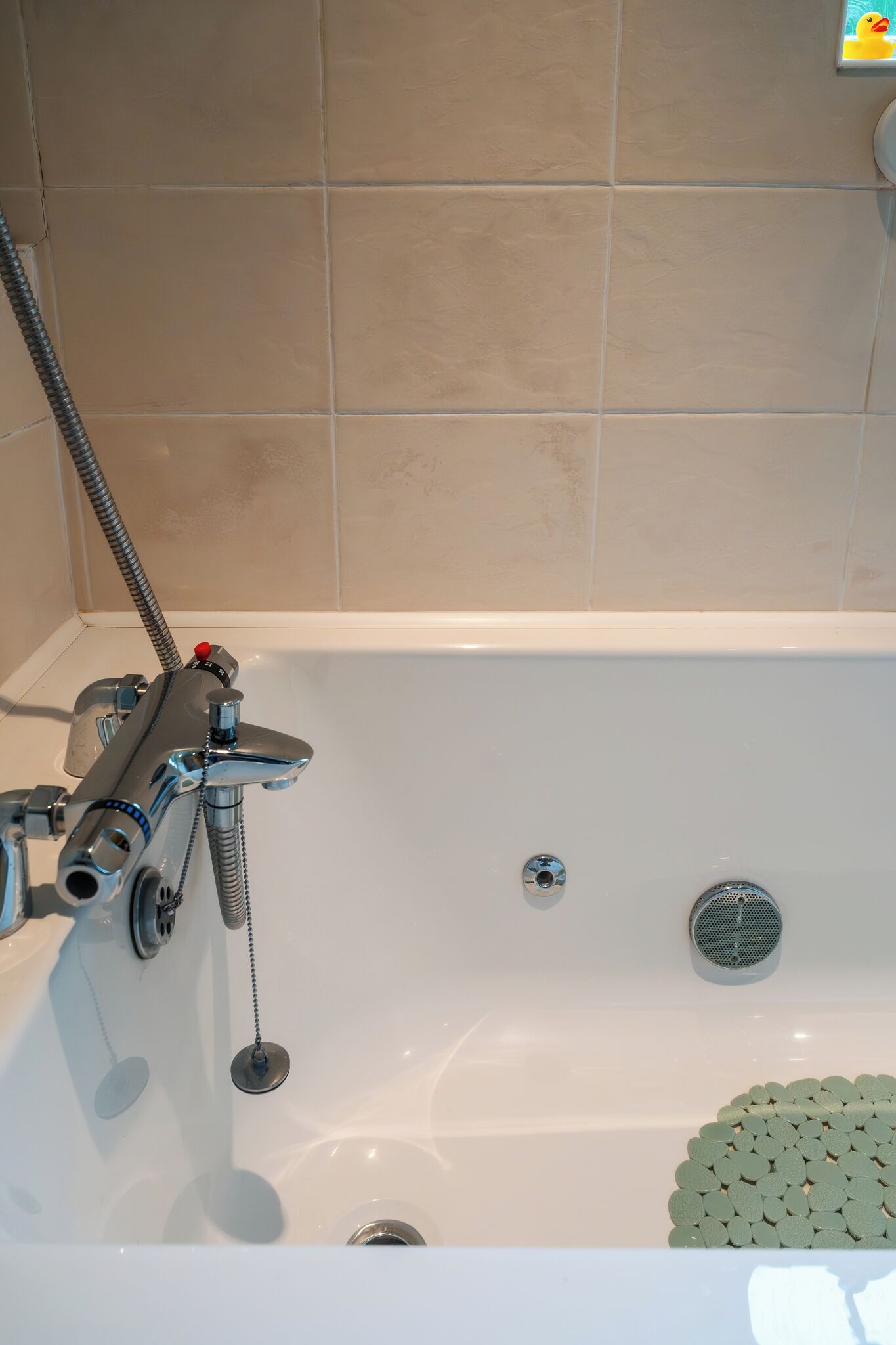 A bathtub with a showerhead, a drain, and a rubber mat.