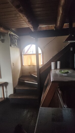 Un escalier menant à une fenêtre offrant une vue, un plafond en bois et un comptoir surmonté d’une assiette verte.