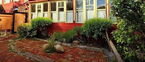 Un edificio rojo con múltiples ventanas, un camino de ladrillo y diversas plantas verdes.