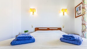 Hotellihuone, jossa on sänky, kaksi seinälle asennettua lamppua, pieni ruukkukasvi ja värikäs verho.