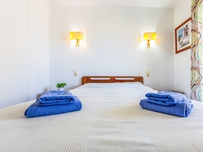 A hotel room with a bed, two wall-mounted lamps, a small potted plant, and a colorful curtain. - Costa Blanca I by Interhome (Cambrils)