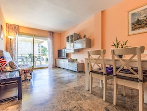 A living room with a sofa, a dining table with chairs, a TV, and a balcony with a view. - Costa Blanca I by Interhome (Cambrils)