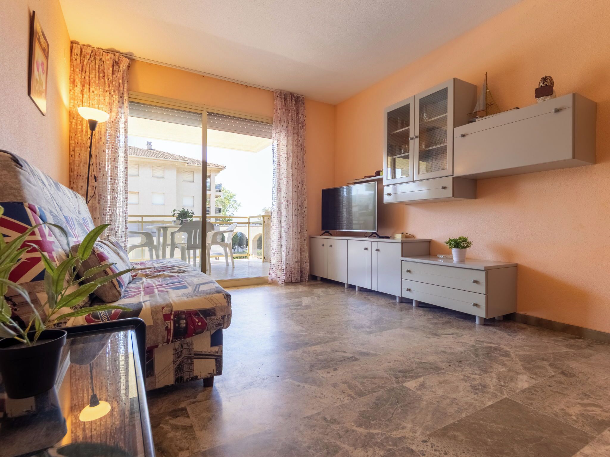 A compact living space with a sofa, a TV, a cabinet, and a balcony with a view of buildings.