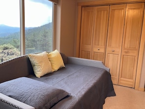 A bedroom with a large window, a bed with a gray bedspread, two pillows, and a wooden wardrobe. - Modern Mountain Haven (Boulder)