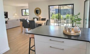 Eine moderne Küche mit einer zentralen Kochinsel, Essbereich mit Stühlen, einer Couch und einem Fernseher.