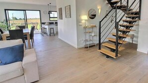Een ruime woonkamer met een moderne trap, een eethoek en uitzicht door grote ramen.