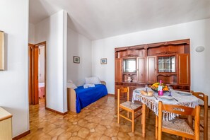 Ein Zimmer mit einem Bett, einem Esstisch mit Tellern, Gläsern und einer Obstschale.
