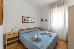 Ein Schlafzimmer mit einem Bett, einem Nachttisch, einem Schreibtisch und einem Fenster mit Vorhängen.