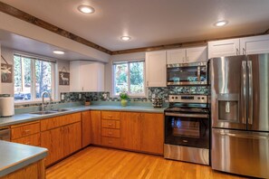 A modern kitchen with wooden cabinets, stainless steel appliances, and a large window. - Adorable High Mountain Retreat with HOTTUB! (Duck Creek Village)