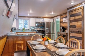 A modern kitchen with white cabinets, stainless steel appliances, and a dining area with wooden chairs and a table set for four. - Adorable High Mountain Retreat with HOTTUB! (Duck Creek Village)