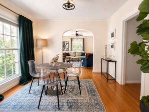 A dining area with a table and chairs, a lamp, and a view through an archway to a living room with a sofa and a ceiling fan. - 2 Bedroom House Near SMU, White Rock Lake, Free Parking (Dallas)