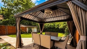 Een terras buiten met een overdekte zithoek, een tafel en stoelen.