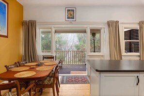 A dining area with a wooden table, chairs, and a view of the outdoors through large windows. - Tranquil Cottage | Lovely Street, Walk to Leura (Leura)