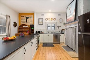 A modern kitchen with white cabinets, a stainless steel refrigerator, and a wooden floor. - Tranquil Cottage | Lovely Street, Walk to Leura (Leura)