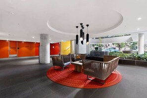 Eine moderne Lobby mit einer Sitzgruppe in Kreisform, einer gelben Akzentwand und Blick ins Freie.